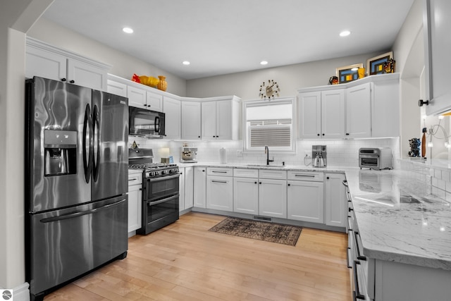 kitchen with black appliances, a sink, white cabinets, decorative backsplash, and recessed lighting