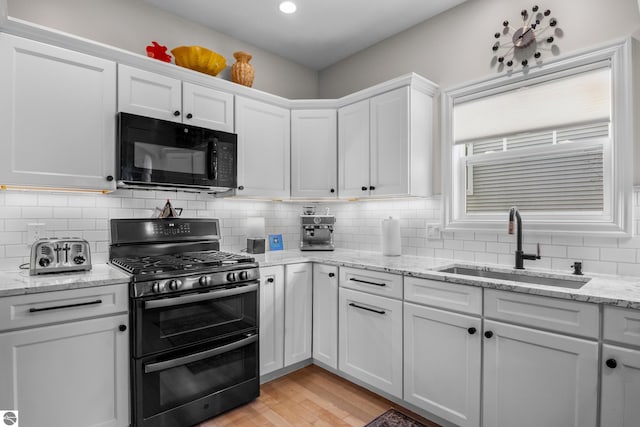 kitchen featuring black microwave, double oven range, a sink, white cabinetry, and light wood-type flooring