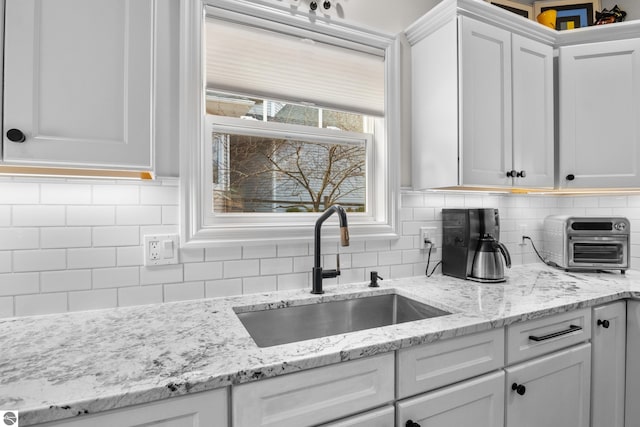 kitchen featuring a sink, white cabinets, decorative backsplash, and light stone countertops