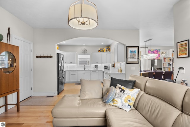 living area with arched walkways, light wood-type flooring, and baseboards