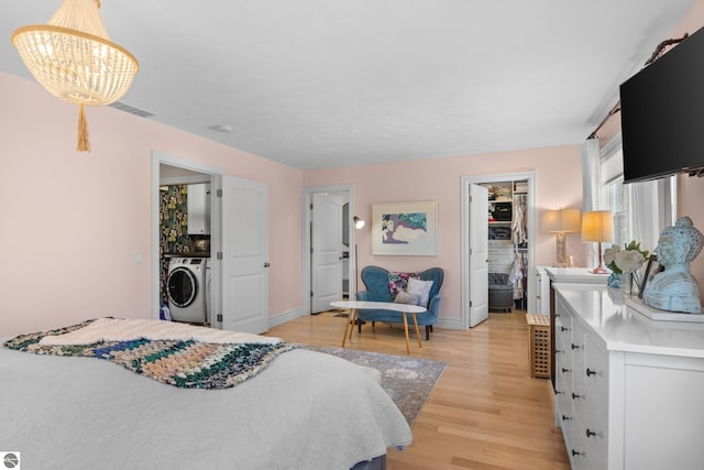 bedroom featuring washer / clothes dryer, a chandelier, light wood-style floors, baseboards, and a walk in closet