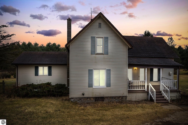 rear view of property with covered porch, roof with shingles, and a lawn