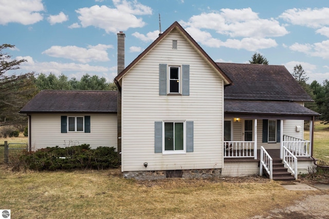 back of property with a shingled roof, a chimney, a porch, and a yard
