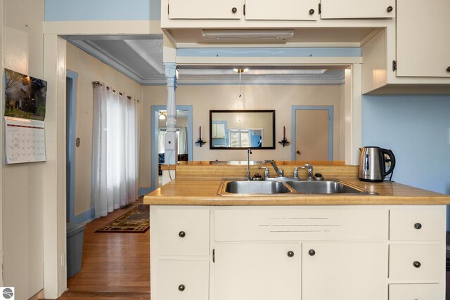 kitchen featuring white cabinetry, light countertops, a sink, a peninsula, and wood finished floors