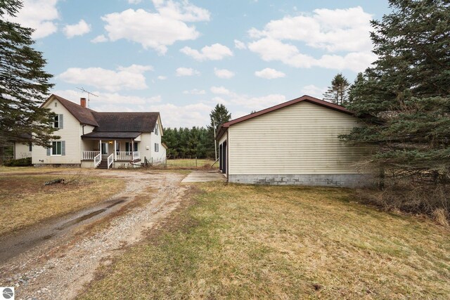 view of side of home with roof with shingles, dirt driveway, a porch, a yard, and a chimney