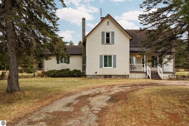 view of front of house with dirt driveway, a chimney, a front lawn, roof with shingles, and covered porch