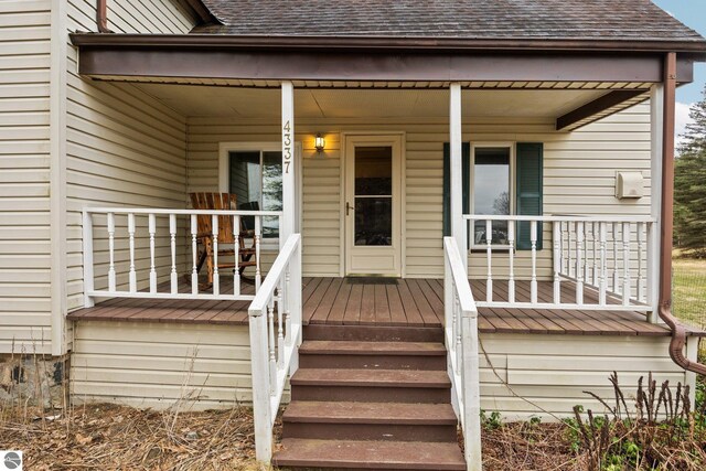 entrance to property with a porch and a shingled roof