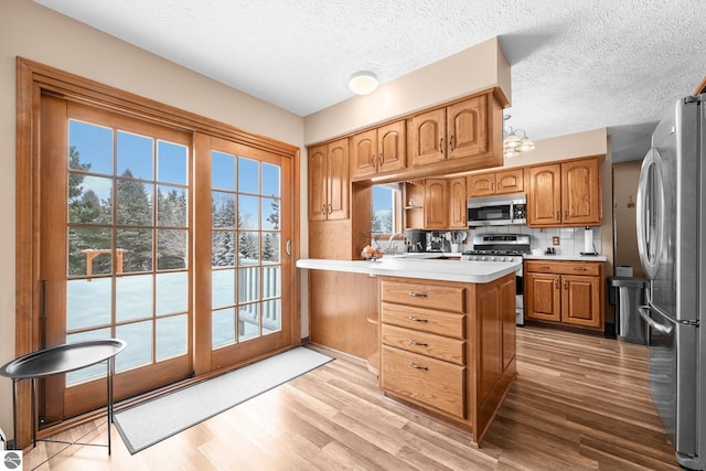 800 Evart St, Cadillac, MI 49601 - kitchen with a peninsula, light countertops, a textured ceiling, light wood-style flooring, and stainless steel appliances