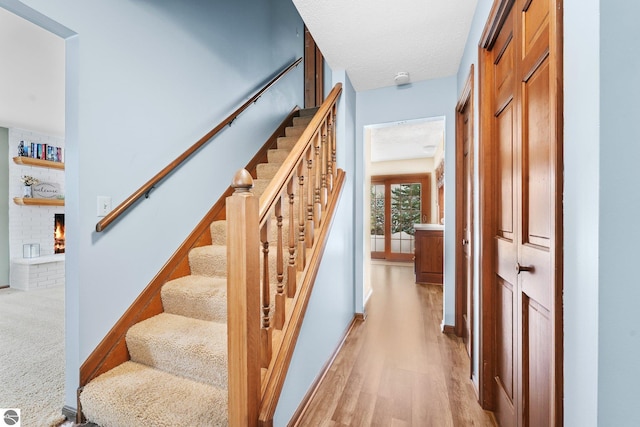 800 Evart St, Cadillac, MI 49601 - staircase featuring a textured ceiling, a brick fireplace, and wood finished floors