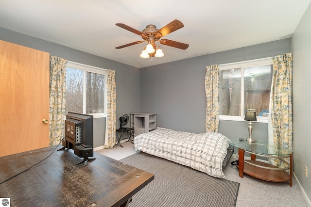 bedroom with baseboards, a wood stove, carpet flooring, and a ceiling fan