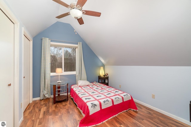 bedroom with a closet, baseboards, wood finished floors, a ceiling fan, and vaulted ceiling