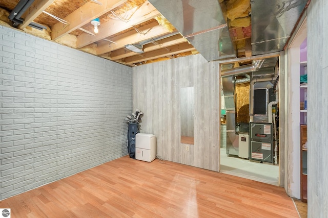 unfinished basement featuring heating unit, brick wall, and wood finished floors