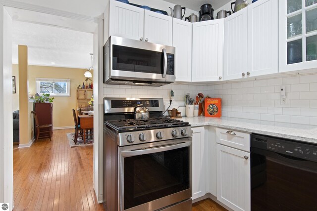 112 N Benzie Blvd, Beulah, MI 49617 - kitchen with white cabinetry, stainless steel appliances, decorative backsplash, light stone counters, and light wood-style flooring