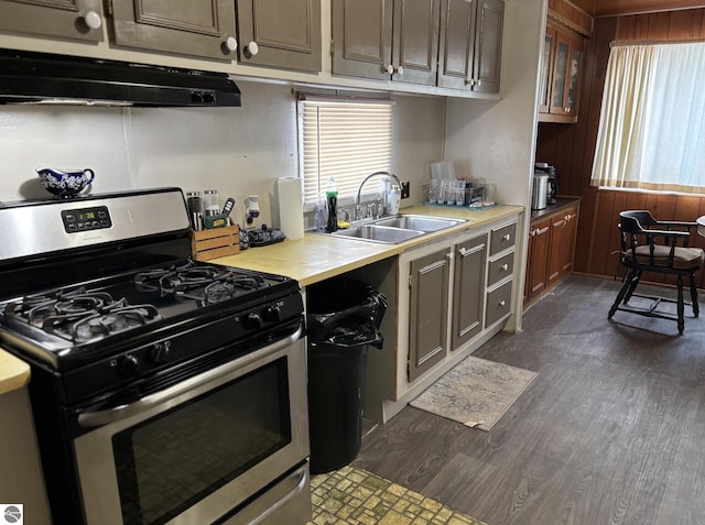kitchen with light countertops, a sink, under cabinet range hood, stainless steel range with gas cooktop, and dark wood-type flooring
