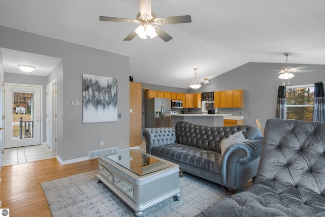 living area with lofted ceiling, light wood-type flooring, baseboards, visible vents, and ceiling fan
