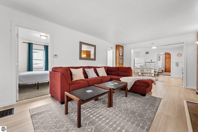 living area featuring arched walkways, visible vents, crown molding, and wood finished floors