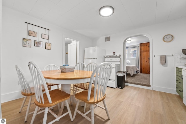 dining space featuring baseboards, light wood-type flooring, visible vents, and arched walkways