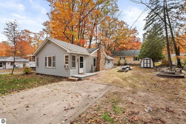 back of house featuring an outbuilding, a fire pit, a chimney, and a shed