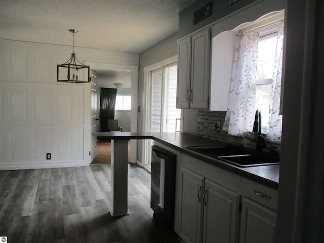 kitchen featuring dishwashing machine, dark wood-type flooring, a sink, dark countertops, and backsplash