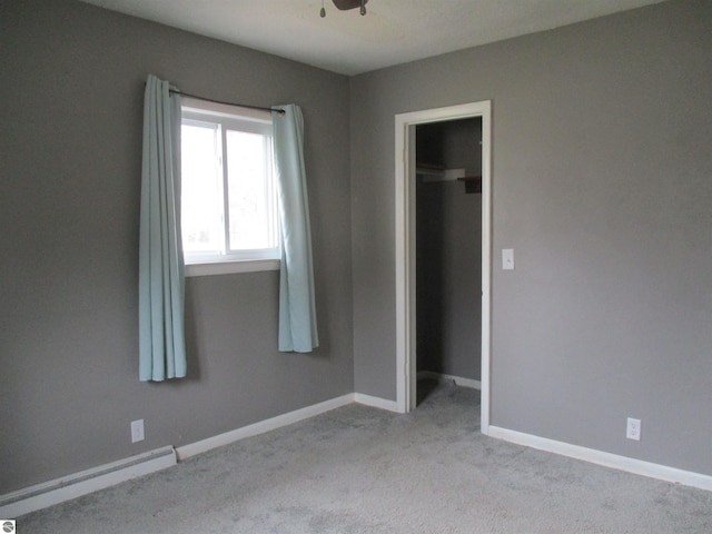 unfurnished bedroom with light carpet, a baseboard heating unit, baseboards, and a spacious closet