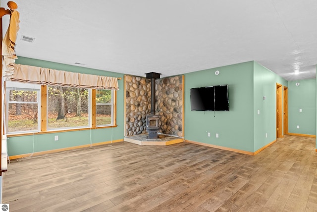 unfurnished living room with a wood stove, visible vents, baseboards, and wood finished floors
