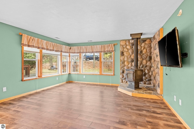 unfurnished living room featuring a wood stove, baseboards, and wood finished floors