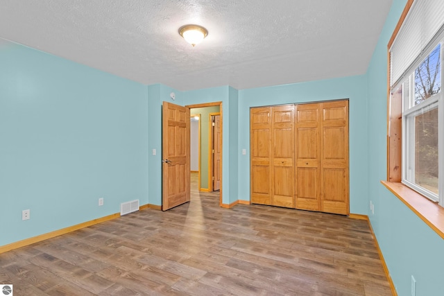 unfurnished bedroom featuring a textured ceiling, a closet, visible vents, wood finished floors, and baseboards