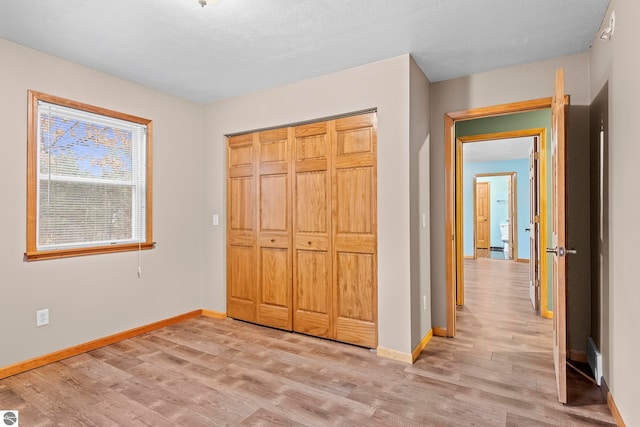 unfurnished bedroom featuring a closet, light wood-type flooring, and baseboards