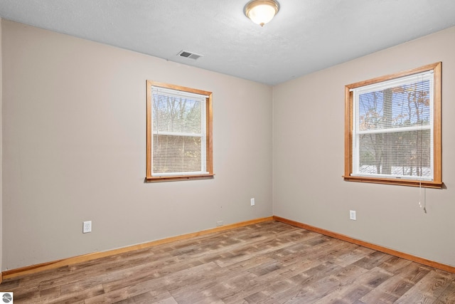 spare room with a textured ceiling, wood finished floors, baseboards, and visible vents