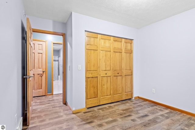 unfurnished bedroom with a textured ceiling, wood finished floors, baseboards, and a closet