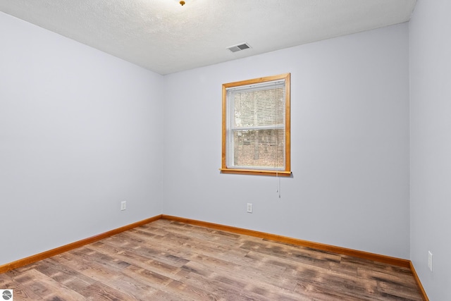 spare room with visible vents, baseboards, wood finished floors, and a textured ceiling