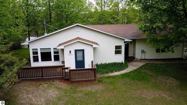 12110 Jonathan Dr, Rapid City, MI 49676 - view of front of house featuring a shingled roof, a front yard, and a wooden deck