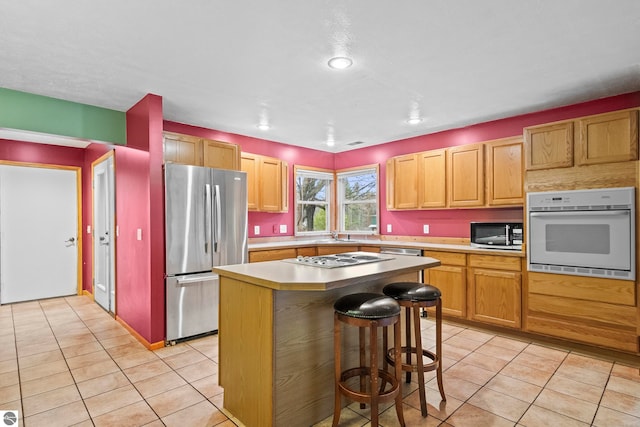 kitchen with a breakfast bar, light countertops, a kitchen island, light tile patterned flooring, and stainless steel appliances