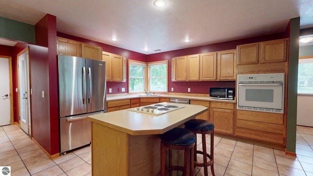 12110 Jonathan Dr, Rapid City, MI 49676 - kitchen featuring appliances with stainless steel finishes, light tile patterned flooring, light countertops, a breakfast bar, and a kitchen island