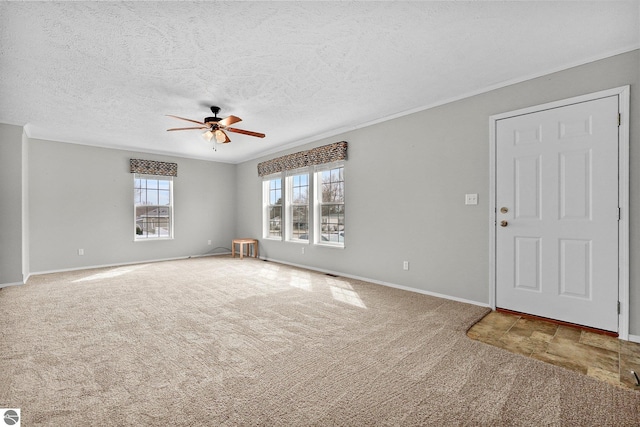 unfurnished living room with baseboards, a ceiling fan, a textured ceiling, crown molding, and carpet flooring
