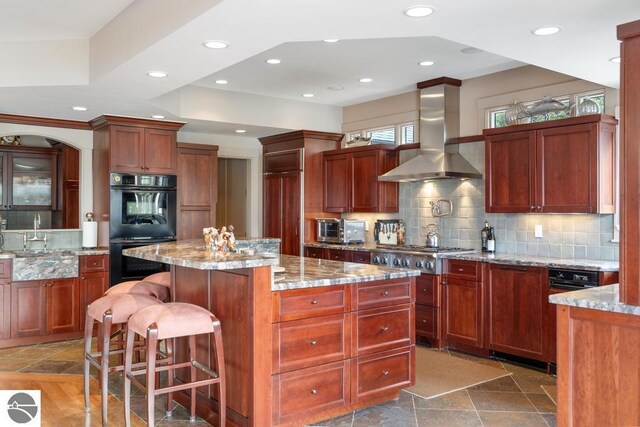 6579 Woods Creek Dr, Charlevoix, MI 49720 - kitchen with dobule oven black, wall chimney range hood, stainless steel gas cooktop, a sink, and stone tile flooring