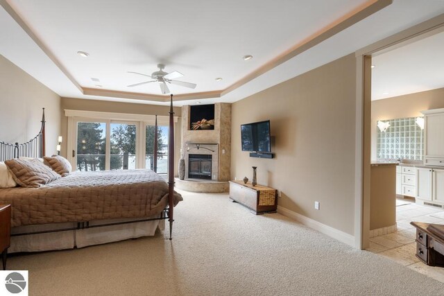 6579 Woods Creek Dr, Charlevoix, MI 49720 - bedroom with baseboards, a large fireplace, access to exterior, a tray ceiling, and light colored carpet