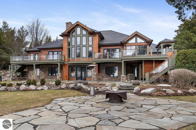 6579 Woods Creek Dr, Charlevoix, MI 49720 - rear view of house featuring a fire pit, stone siding, a chimney, a patio, and a balcony