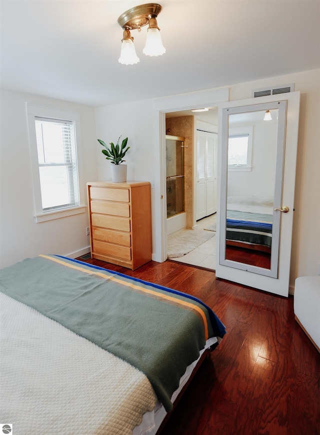 bedroom featuring connected bathroom, hardwood / wood-style floors, visible vents, and a closet