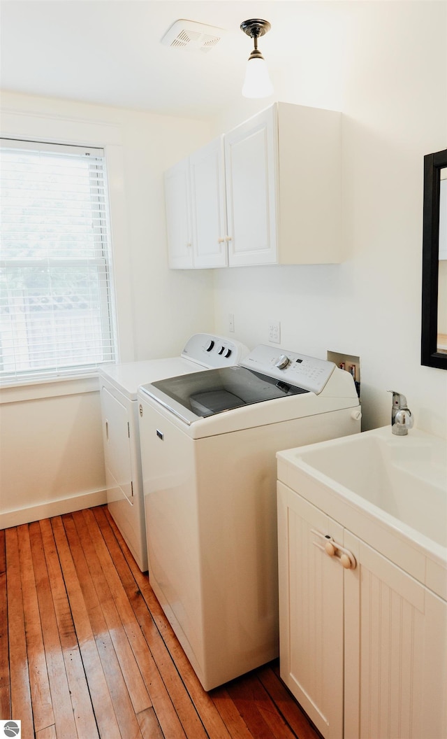 laundry room featuring washing machine and clothes dryer, light wood-style flooring, visible vents, and cabinet space