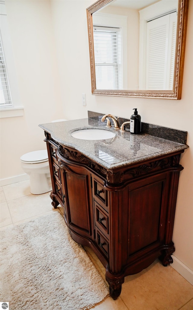 half bath with toilet, vanity, tile patterned floors, and baseboards
