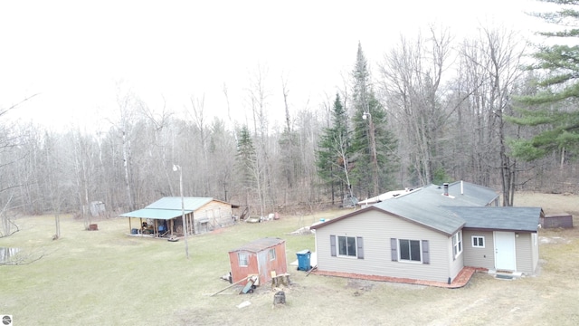 exterior space featuring a detached carport, a front lawn, an outdoor structure, and a wooded view