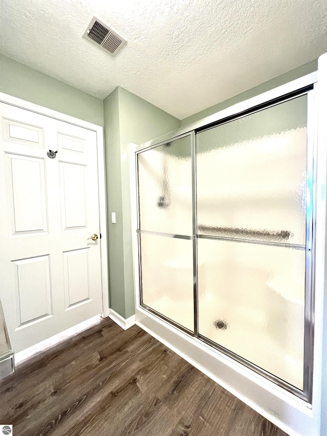 624 S Lake St, Cadillac, MI 49601 - bathroom featuring visible vents, baseboards, a textured ceiling, wood finished floors, and a shower with shower door