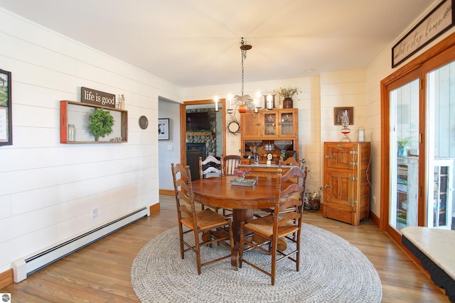dining room featuring baseboards, light wood-type flooring, an inviting chandelier, and a baseboard heating unit