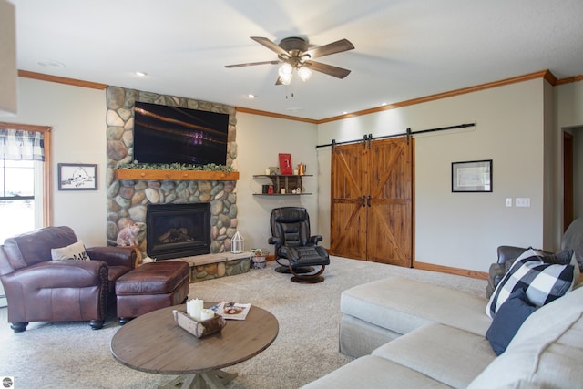 carpeted living area with baseboards, a stone fireplace, ornamental molding, a ceiling fan, and a barn door