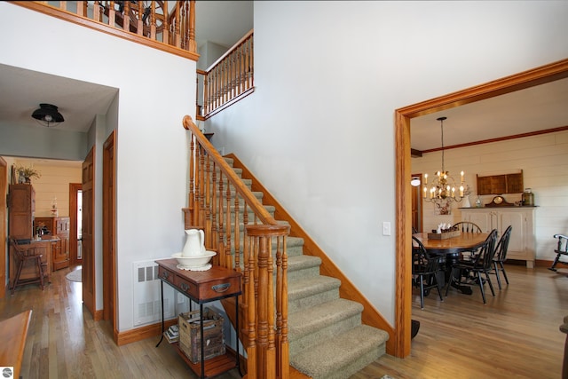 stairway with a chandelier, wooden walls, a high ceiling, visible vents, and wood finished floors