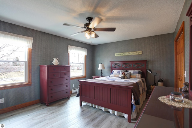 bedroom with a textured ceiling, a baseboard heating unit, wallpapered walls, light wood finished floors, and baseboards