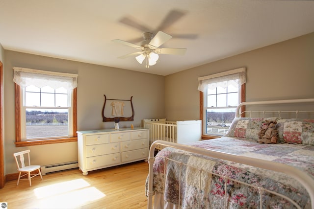 bedroom with light wood finished floors, a baseboard radiator, and a ceiling fan