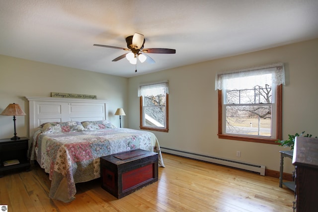 bedroom featuring light wood-type flooring, multiple windows, a baseboard heating unit, and ceiling fan