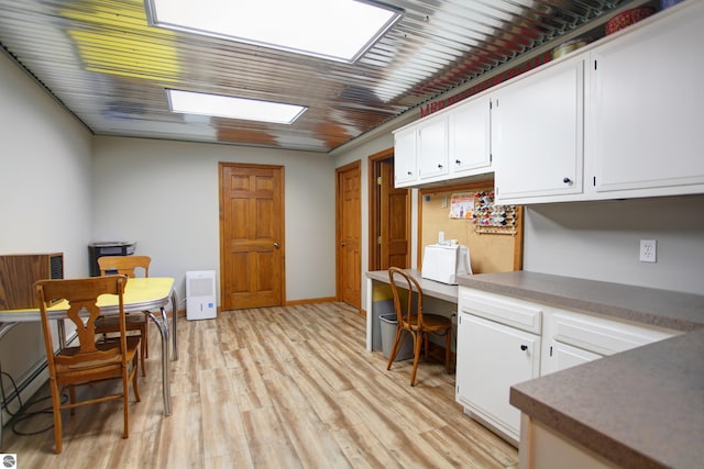office space featuring built in desk, light wood-style floors, baseboard heating, and a skylight